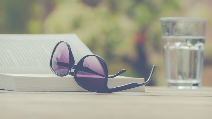 Kleine dingen in het leven. Een boek, zonnebril en glas water op tafel