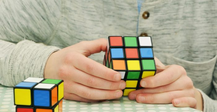 Een persoon met twee Rubiks cubes, waarvan er een in de handen is en nogal moeilijk op te lossen is.